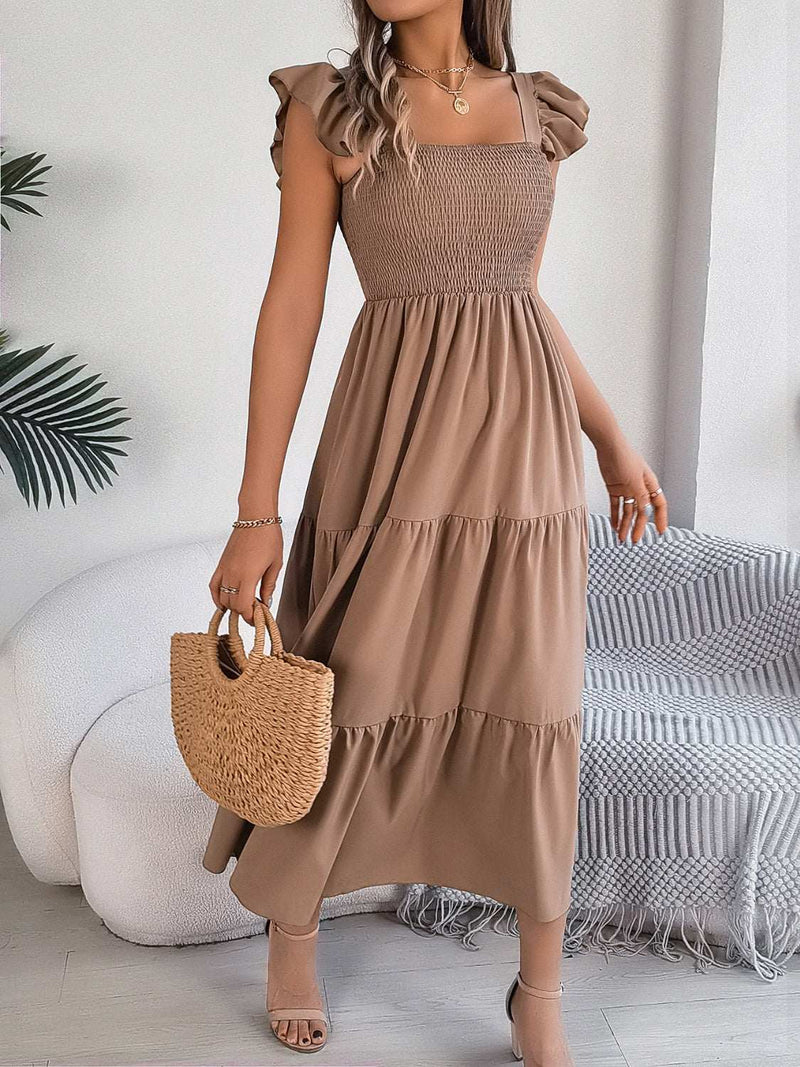 Smocked square neck cap sleeve midi dress in brown, featuring a tiered skirt, worn by woman holding a woven handbag.