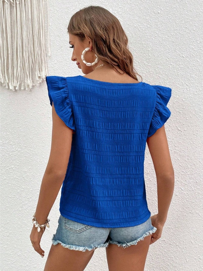 Ruffled square neck cap sleeve blouse in blue with textured fabric, worn by woman with denim shorts.