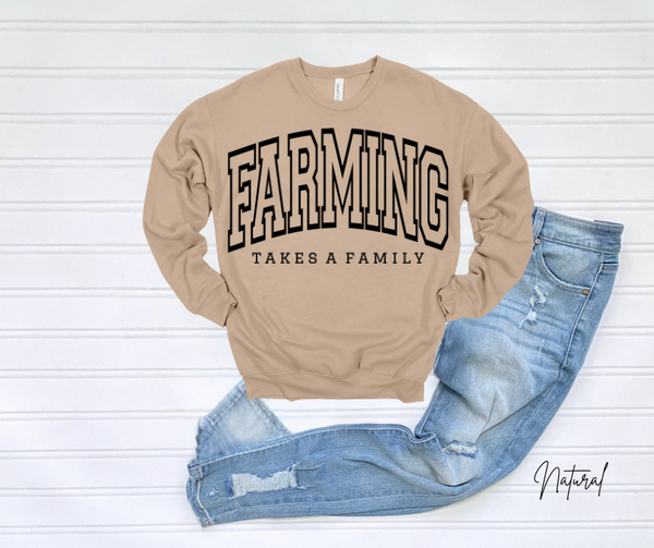 Beige farming sweatshirt with the phrase "Farming Takes a Family" laid over blue jeans.