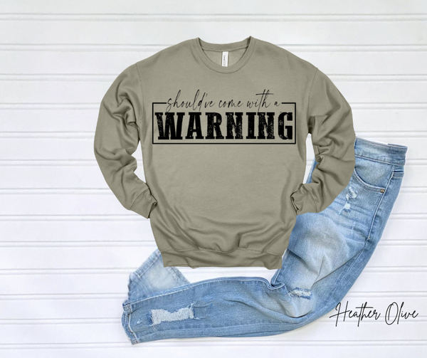 Warning Sweatshirt with bold lettering displayed on white surface alongside blue jeans.