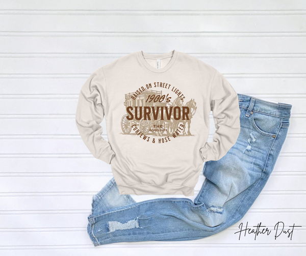 Survivor Sweatshirt displayed on white surface with denim jeans.