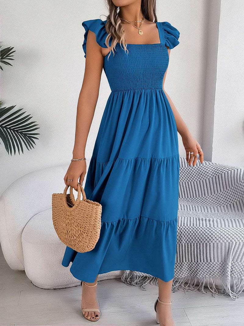 Smocked square neck cap sleeve midi dress in blue, styled with a woven handbag.