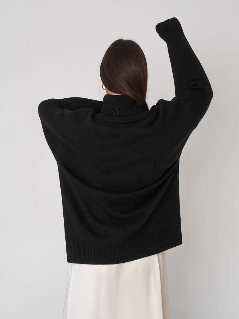 Turtleneck long sleeve sweater in black, slightly stretchy, worn by a person facing away.