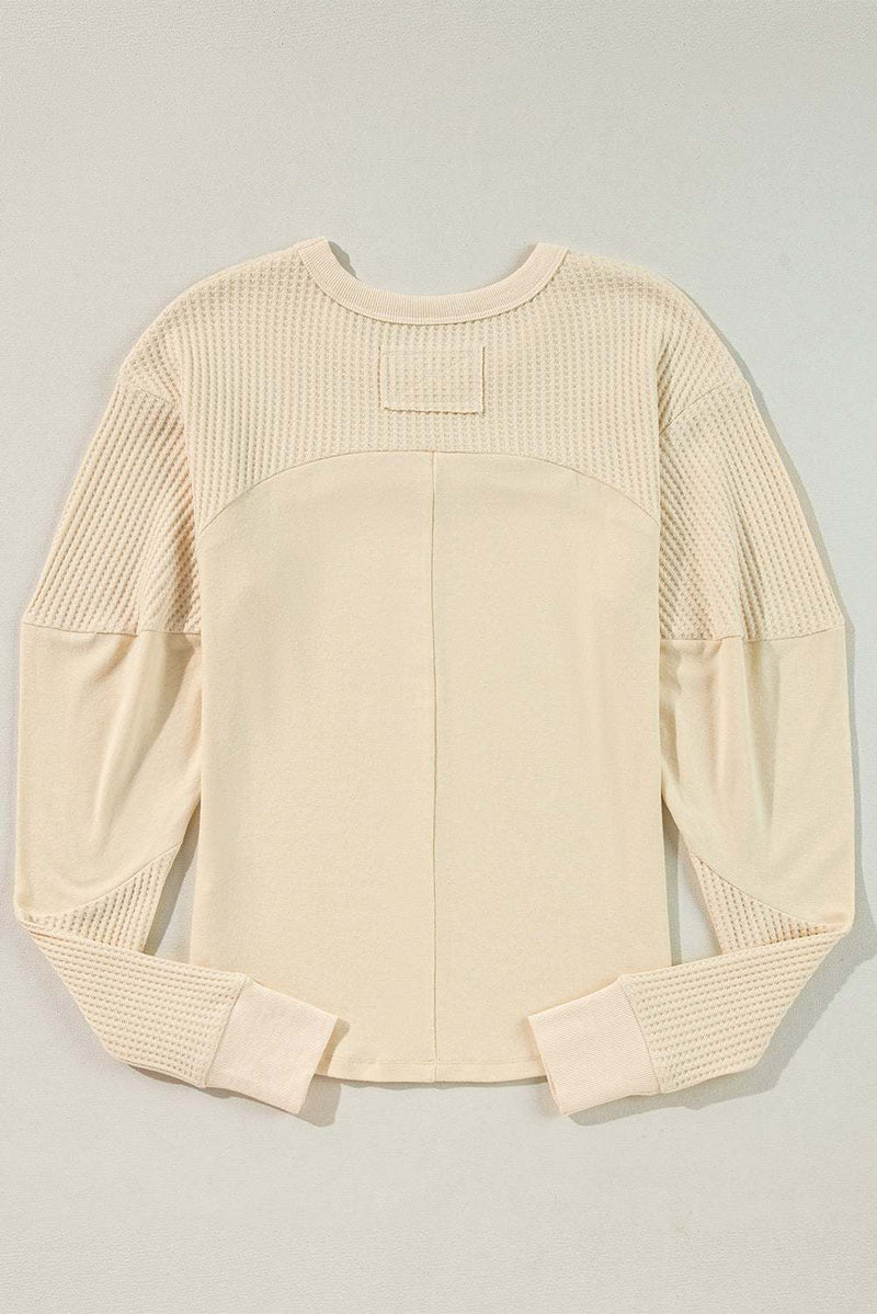 Beige thermal knit top with patchwork, exposed seams, and long sleeves.