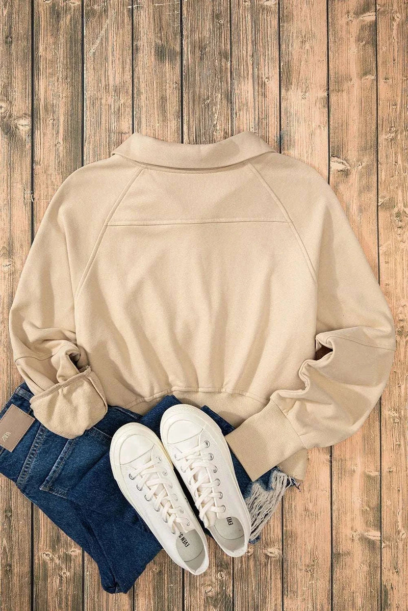 Beige half zip long sleeve sweatshirt with jeans and white sneakers on wooden floor.