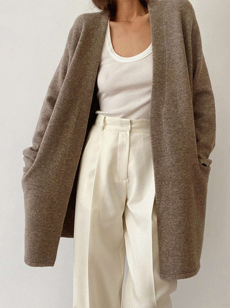 Open front long sleeve cardigan with pockets in brown, worn with white pants and tank top.