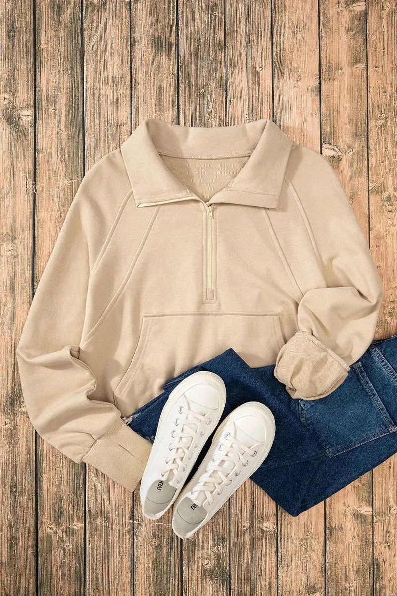 Beige half zip long sleeve sweatshirt on wooden background, paired with jeans and white sneakers.