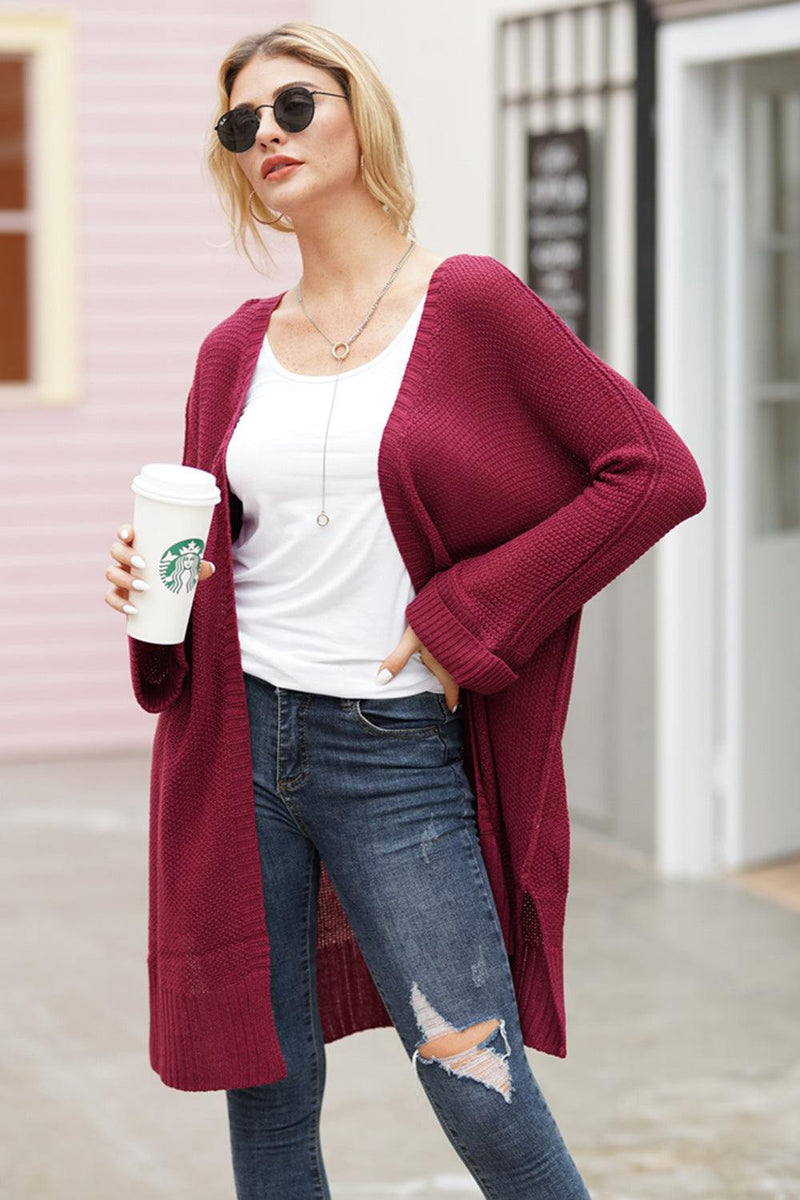 Woman wearing a burgundy open front long sleeve cardigan with jeans, holding a coffee cup.