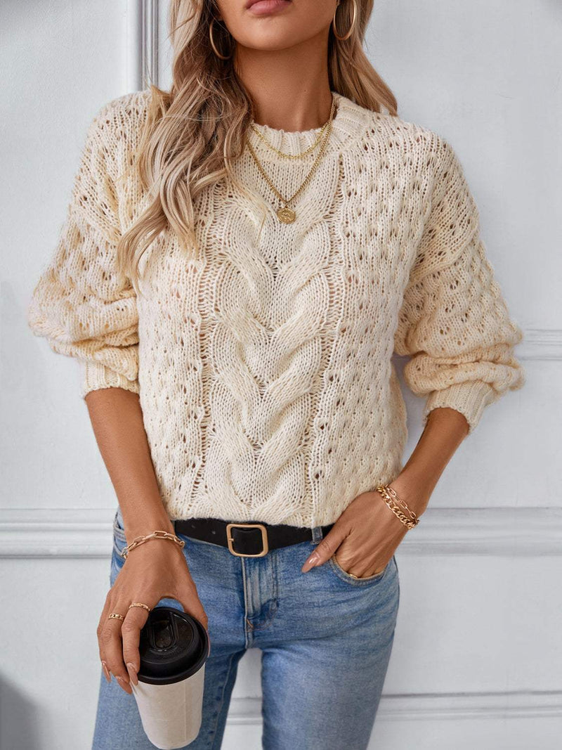 Cable-knit round neck long sleeve sweater in a classic design, worn by a woman with jeans, accessorized with necklaces and holding a coffee.