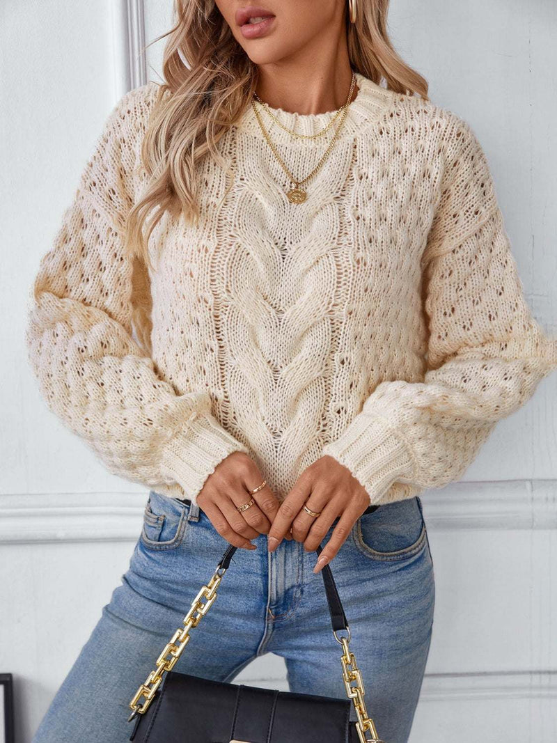 Cable-knit round neck long sleeve sweater in beige, styled with jeans.