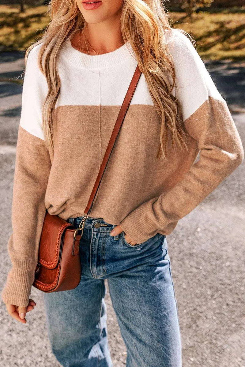 Color block round neck long sleeve sweater in beige and white, worn by a woman with blue jeans and a brown crossbody bag.