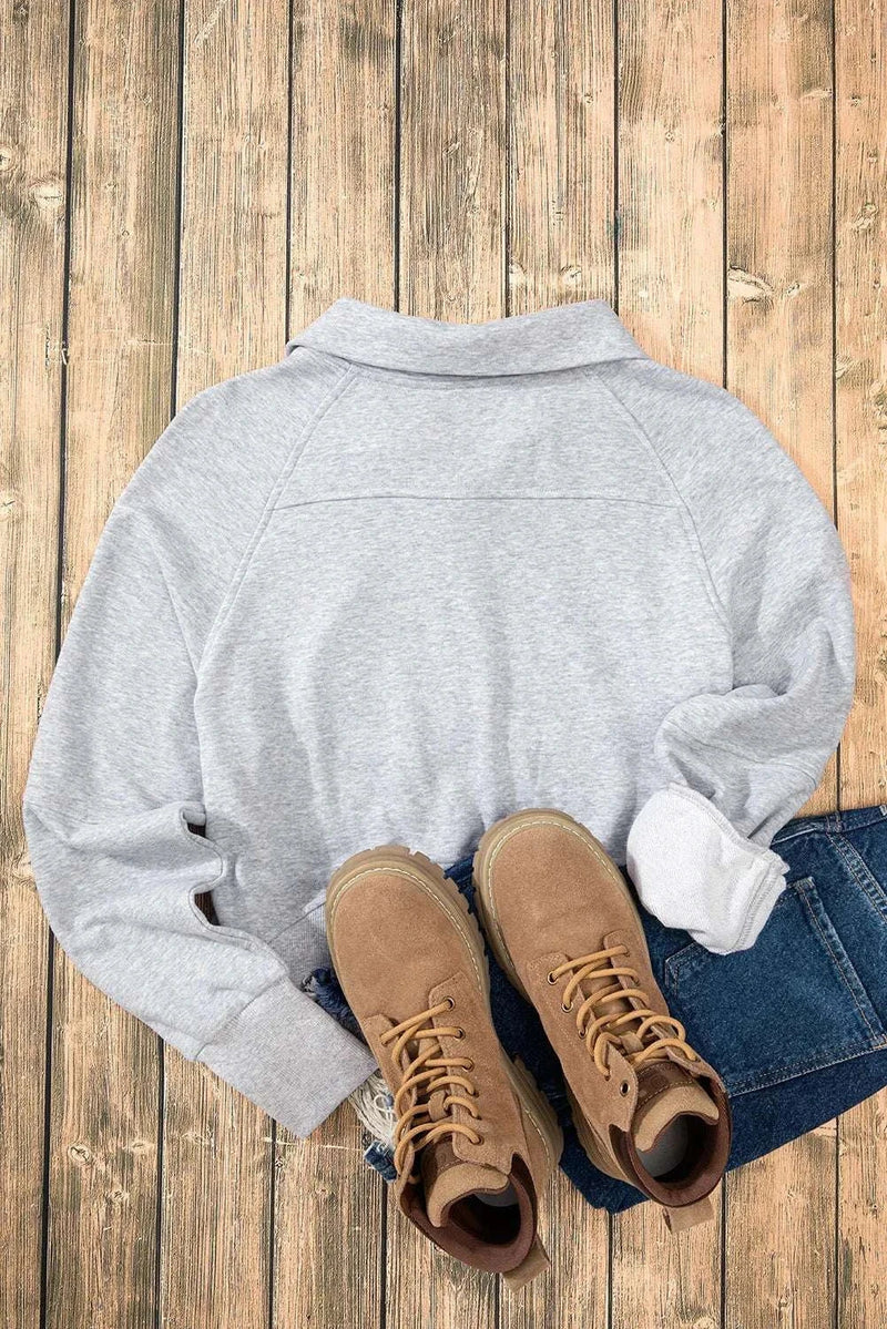 Gray half zip long sleeve sweatshirt on a wooden floor with brown boots and blue jeans.