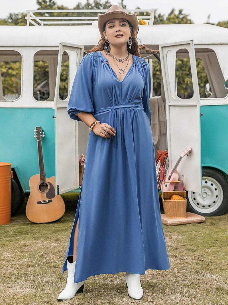 Plus size blue ruched slit three-quarter sleeve midi dress with white boots, outdoor setting.