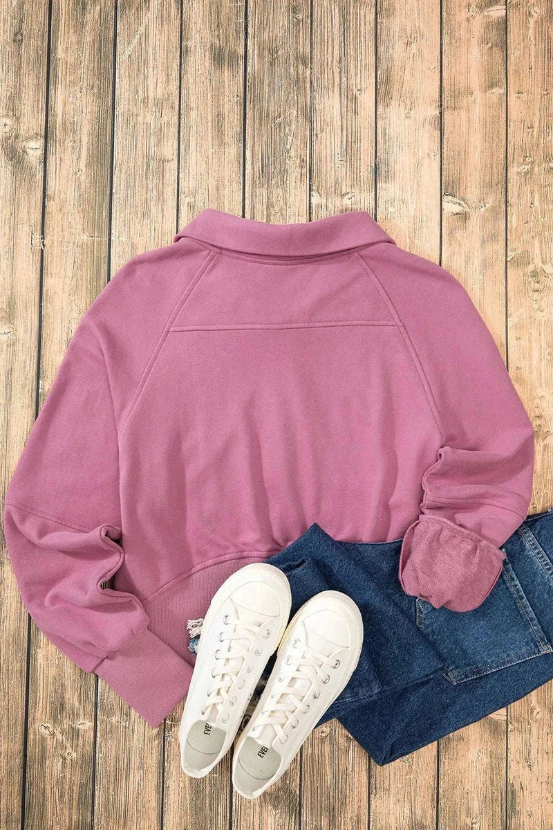 Pink half zip long sleeve sweatshirt on a wooden floor with jeans and white sneakers.