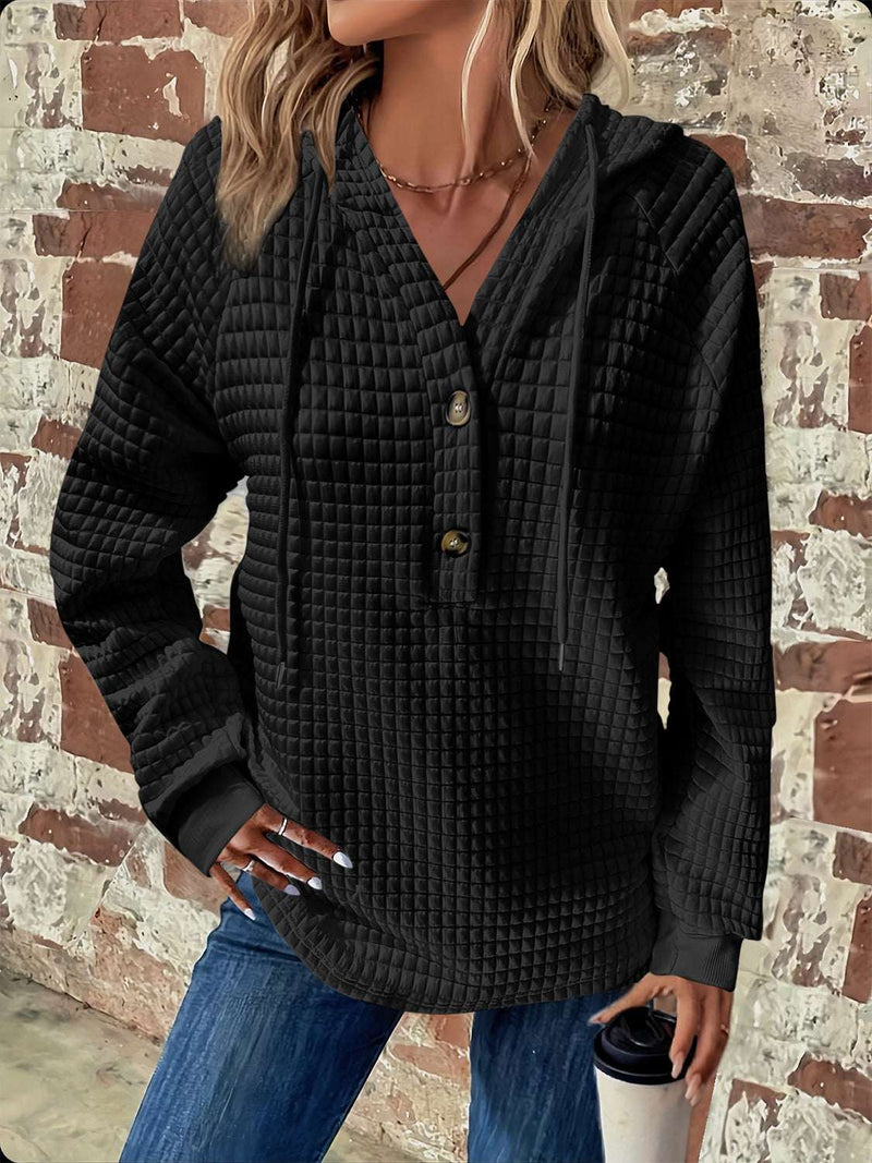 Full size black textured hoodie with button detail and drawstring, long sleeves, worn by model against brick wall.