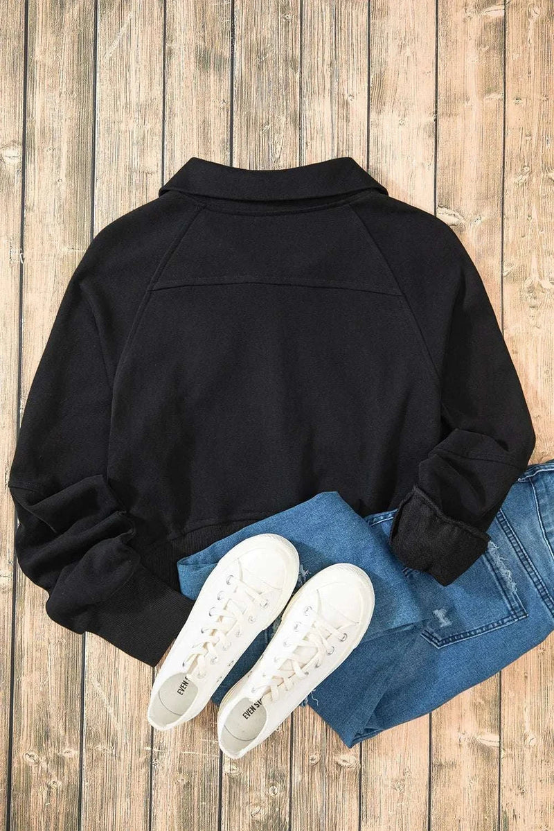 Black half zip long sleeve sweatshirt with jeans and white sneakers on wooden floor.