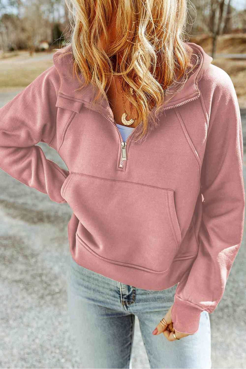 Woman wearing a casual half-zip hoodie with thumbhole sleeves and pockets.